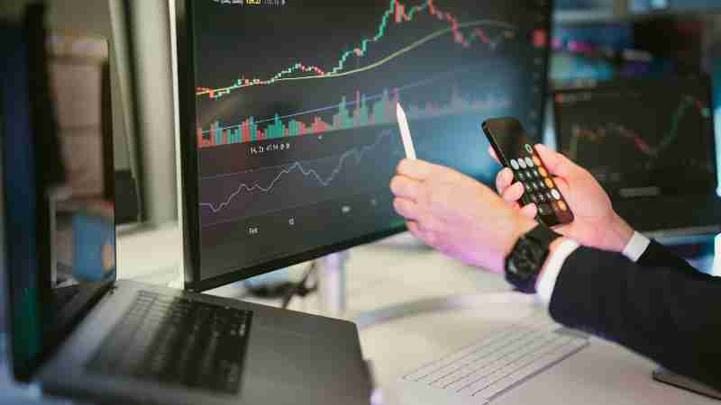 A professional analyzing financial charts on computer monitors and a smartphone, symbolizing digital finance strategies., tags: von - pexel